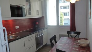 A compact kitchen with white cabinets, a black countertop, a built-in oven, and a coffee maker. There is a window with blinds and a table with chairs. - APARTMENT FOR 2 OR 3 PERS THONON CENTER (Thonon-Les-Bains)