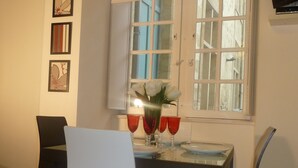 Un comedor con una mesa dispuesta para dos personas, un florero con flores blancas y copas de vino tinto.