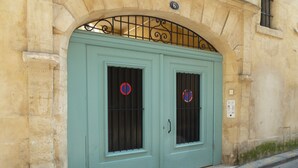 Unas puertas dobles con ventanas de rejas, un arco de metal en la parte superior y un muro de piedra.
