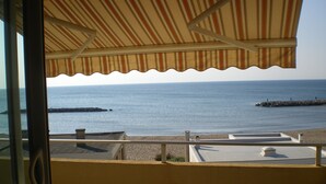 A balcony with a striped awning overlooking a beach with calm waters and a rocky breakwater. - valras-plage luxury apartment top floor first line  (Valras-Plage)
