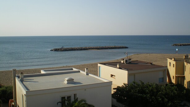 A coastal view with a rocky breakwater, a sandy beach, and buildings with flat roofs. - valras-plage luxury apartment top floor first line  (Valras-Plage)