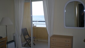 A room with a bed, a wooden dresser, a chair, a lamp, and a view of the sea through a glass door. - valras-plage luxury apartment top floor first line  (Valras-Plage)