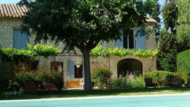 Un edificio de piedra con piscina, mobiliario exterior y un gran árbol en primer plano.