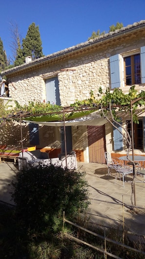 Un bâtiment en pierre doté d’un espace extérieur abrité avec des sièges, d’une pergola couverte de plantes grimpantes et d’un petit jardin.