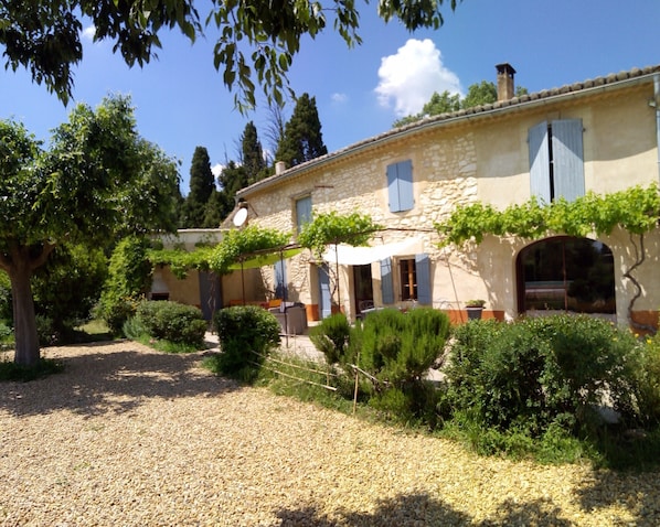 Un bâtiment en pierre avec une allée gravillonnée, entouré de verdure et d’arbres.