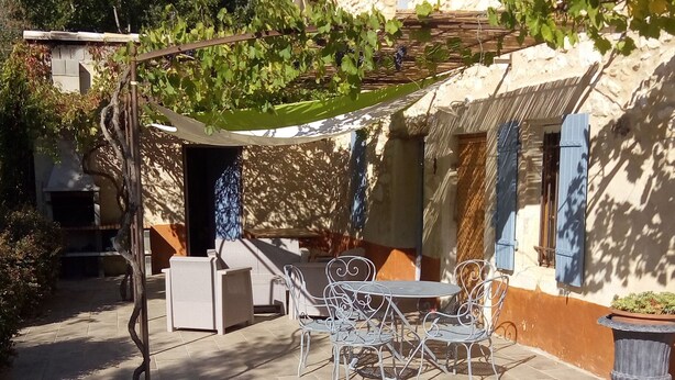 Een binnenplaats met stenen vloer, tuinmeubilair en een pergola begroeid met wijnranken.