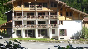 Un edificio de madera de varios pisos con balcones, muros de piedra y montañas al fondo.