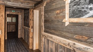 Un pasillo interior de madera con una puerta de madera, suelo de baldosas y un cuadro en la pared.