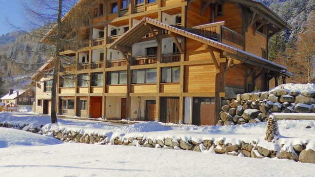 Un edificio de madera de varios pisos con balcones, rodeado de nieve y montañas.