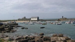 A rocky shoreline with boats docked in a harbor, a building, and a lighthouse in the background. - House with sea view, walking distance to the beach, enclosed garden (Trégunc)
