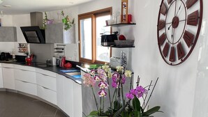 A modern kitchen with white cabinets, a large clock, and a potted orchid plant. - House with sea view, walking distance to the beach, enclosed garden (Trégunc)