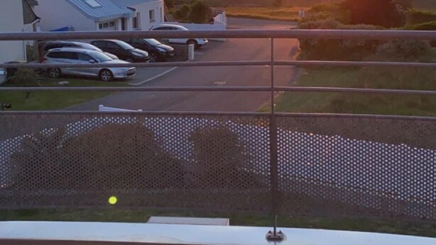 A sunset view from a balcony with a wooden deck, outdoor seating, and a parking area in the background. - House with sea view, walking distance to the beach, enclosed garden (Trégunc)