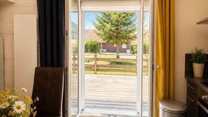 Una habitación con una mesa, una silla, un cubo de basura, un armario y vistas a un patio con un árbol y edificios.