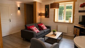 Una sala de estar moderna con un sofá gris, una mesa de centro, una silla, un televisor y una ventana con vistas a zonas verdes.