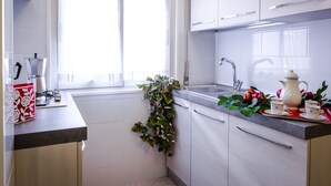 Una cucina moderna con mobili bianchi, un lavandino e una finestra con tende leggere.