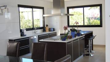 A modern kitchen with a central island, bar stools, and a dining area with a glass table.