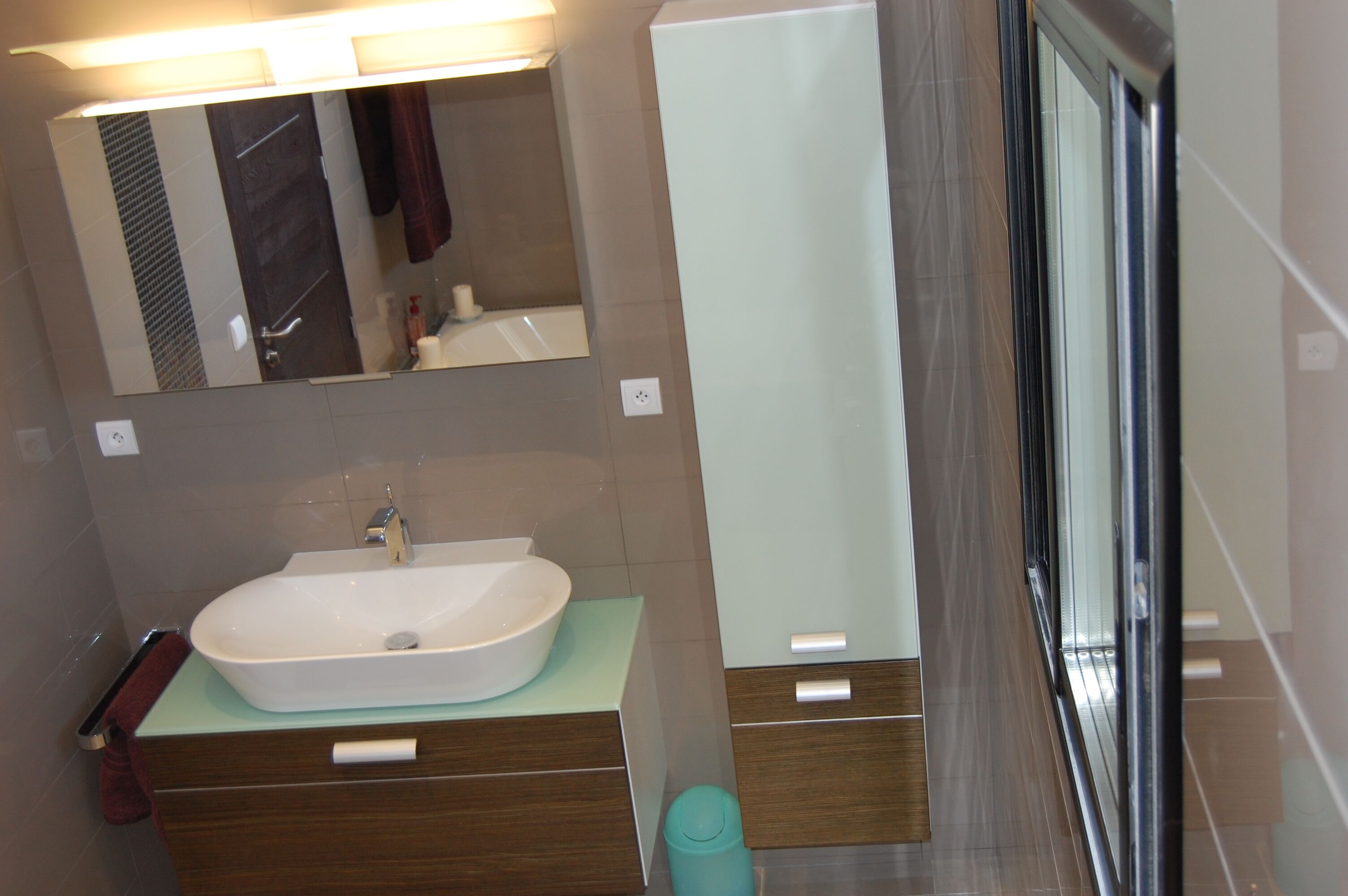 Un baño moderno con un espejo grande, un lavamanos blanco y una cabina de ducha de vidrio.