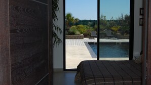 A bedroom with a large sliding glass door leading to a pool area with a patio and various plants. - Direct access to the beach, swimming pool, 8 people, modern 5-star villa (Sète)