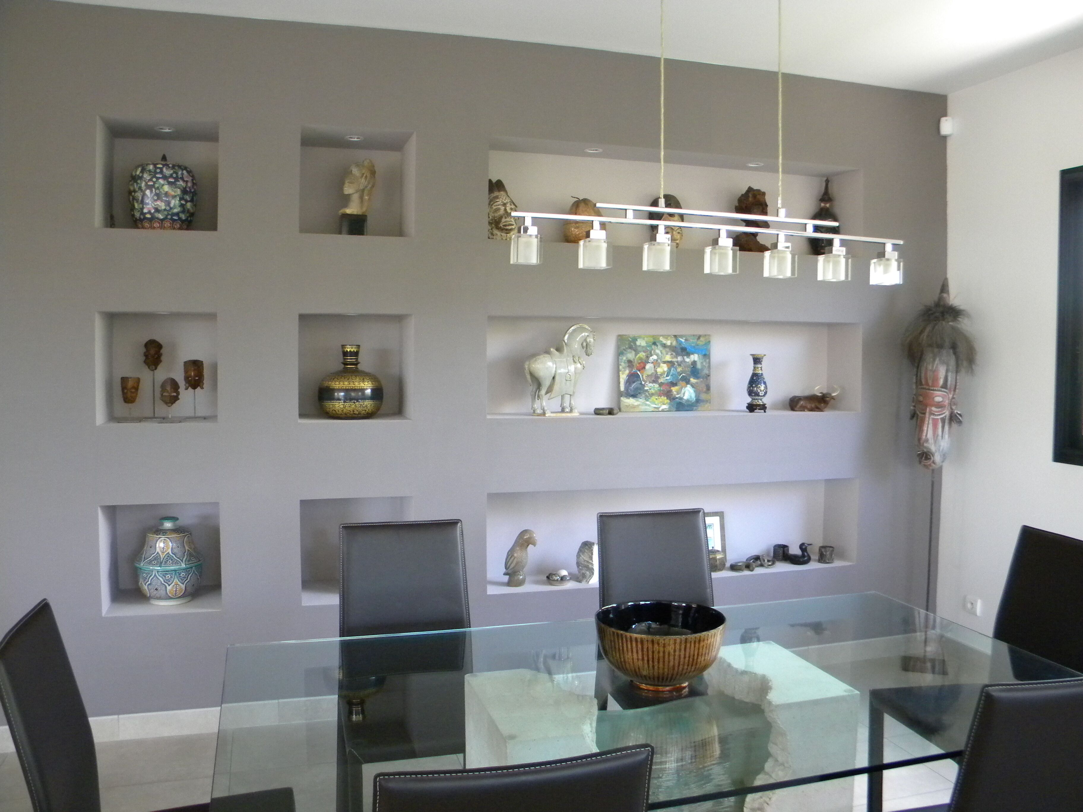 A modern dining area with a glass table and chairs, surrounded by shelves with decorative items.