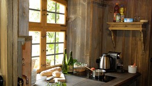 Une cuisine rustique avec des murs en bois, une grande fenêtre, un évier, une machine à café et une étagère remplie de bouteilles et de verres.