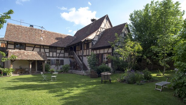 Une maison traditionnelle à colombages, dotée d’une pelouse bien entretenue et d’un espace extérieur aménagé pour s’asseoir.