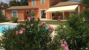 Une maison à deux étages avec une piscine, entourée d’une végétation luxuriante et de plantes en fleurs.