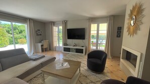 Un salon comprenant un canapé, une table basse, un téléviseur, une cheminée et de grandes fenêtres.
