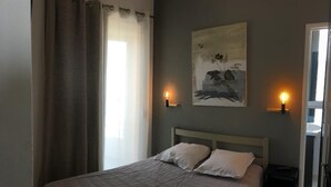 Un dormitorio con cama, dos lámparas de noche, un cuadro en la pared y una ventana con cortinas.