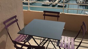 Un balcón con mesa y sillas que da a un puerto deportivo con barcos y un acantilado.