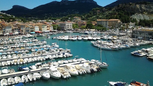 Una marina con numerosos barcos amarrados, rodeada de edificios y montañas al fondo.