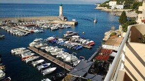 Un puerto deportivo con numerosas embarcaciones amarradas, un faro y edificios al fondo.