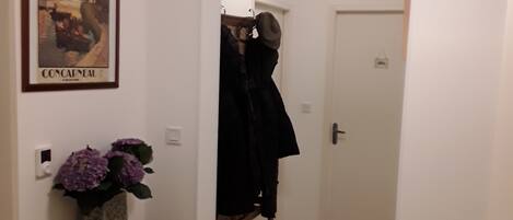 A hallway with a framed poster, a vase of flowers, and a coat rack.