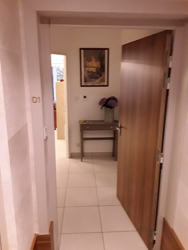 Ein Korridor mit einer Holztür, einem gerahmten Bild an der Wand und einem kleinen Tisch mit einer Blumenvase.