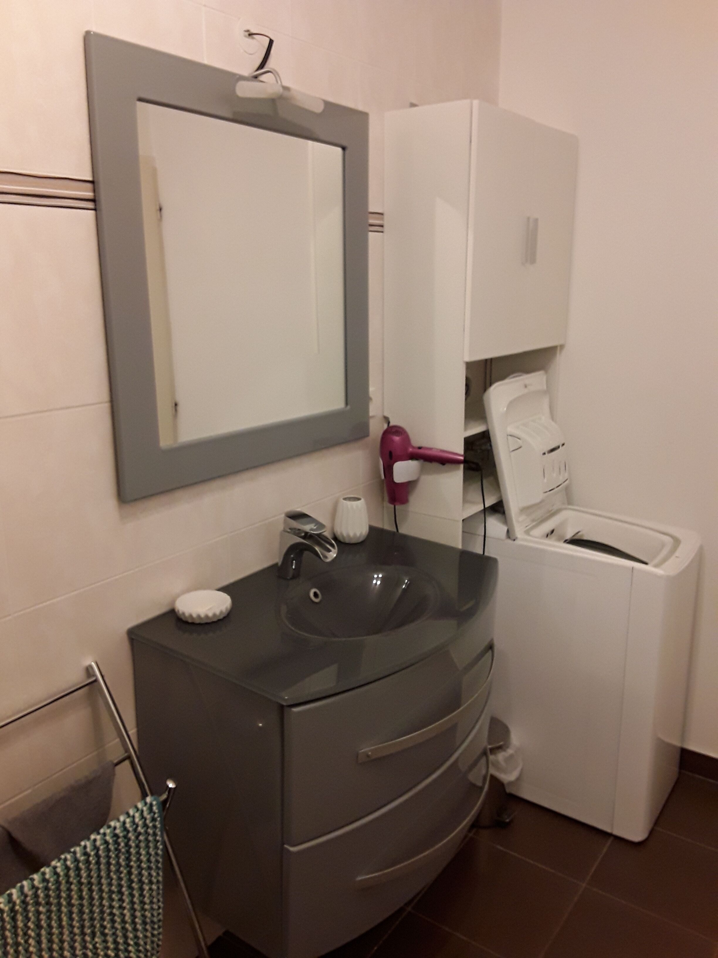 A bathroom with a gray sink, a mirror, a hairdryer, and a white washing machine.