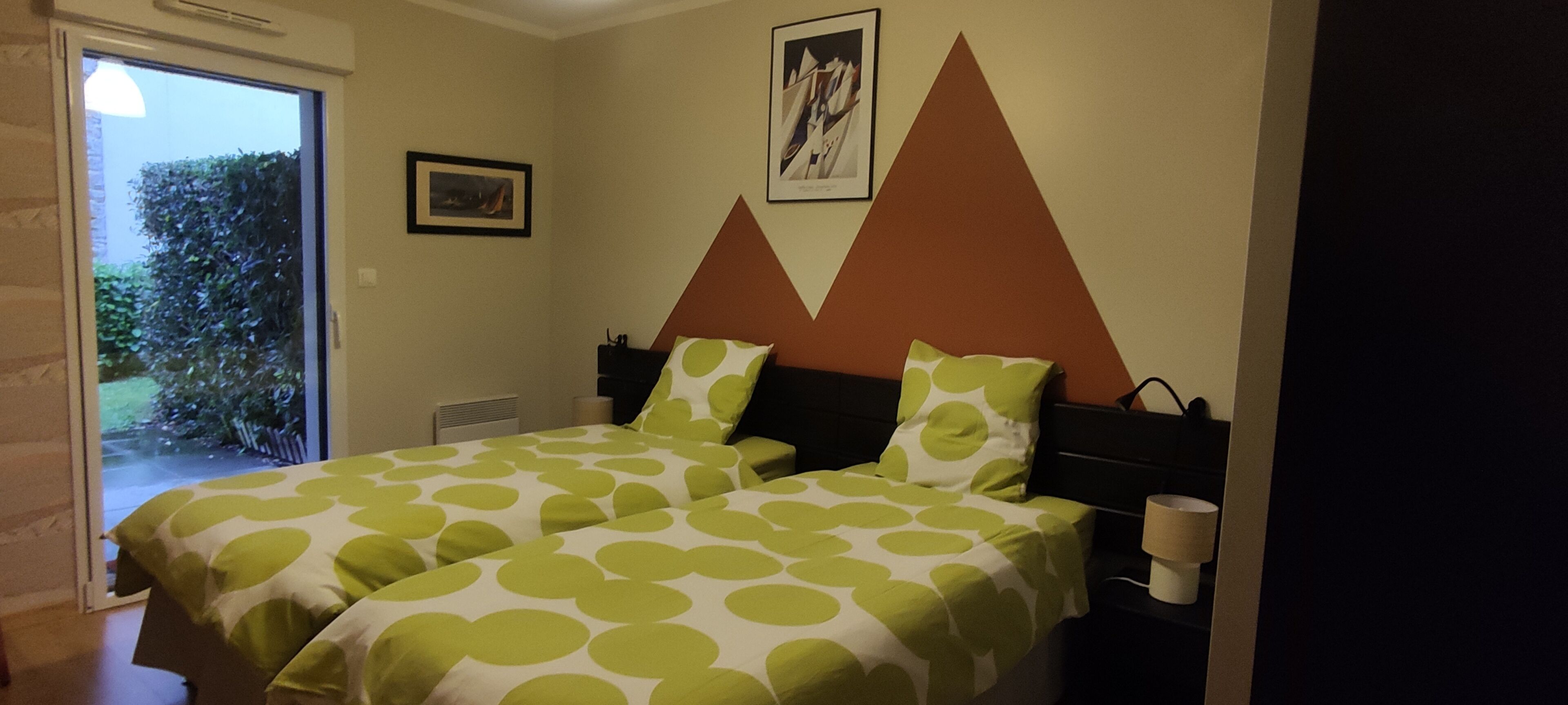 A bedroom with two beds, each with green and white polka dot bedding, a brown headboard, and a framed picture on the wall.
