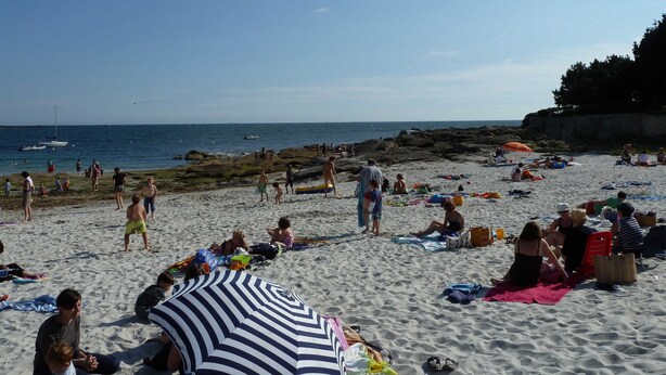 En fyldt strand med folk, der solbader og svømmer.