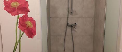 Une cabine de douche dotée d’une porte en verre, d’un pommeau de douche et d’un drain.