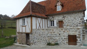 Ein zweistöckiges Steinhaus mit rotem Ziegeldach, Holzbalken und einem kleinen Fenster.
