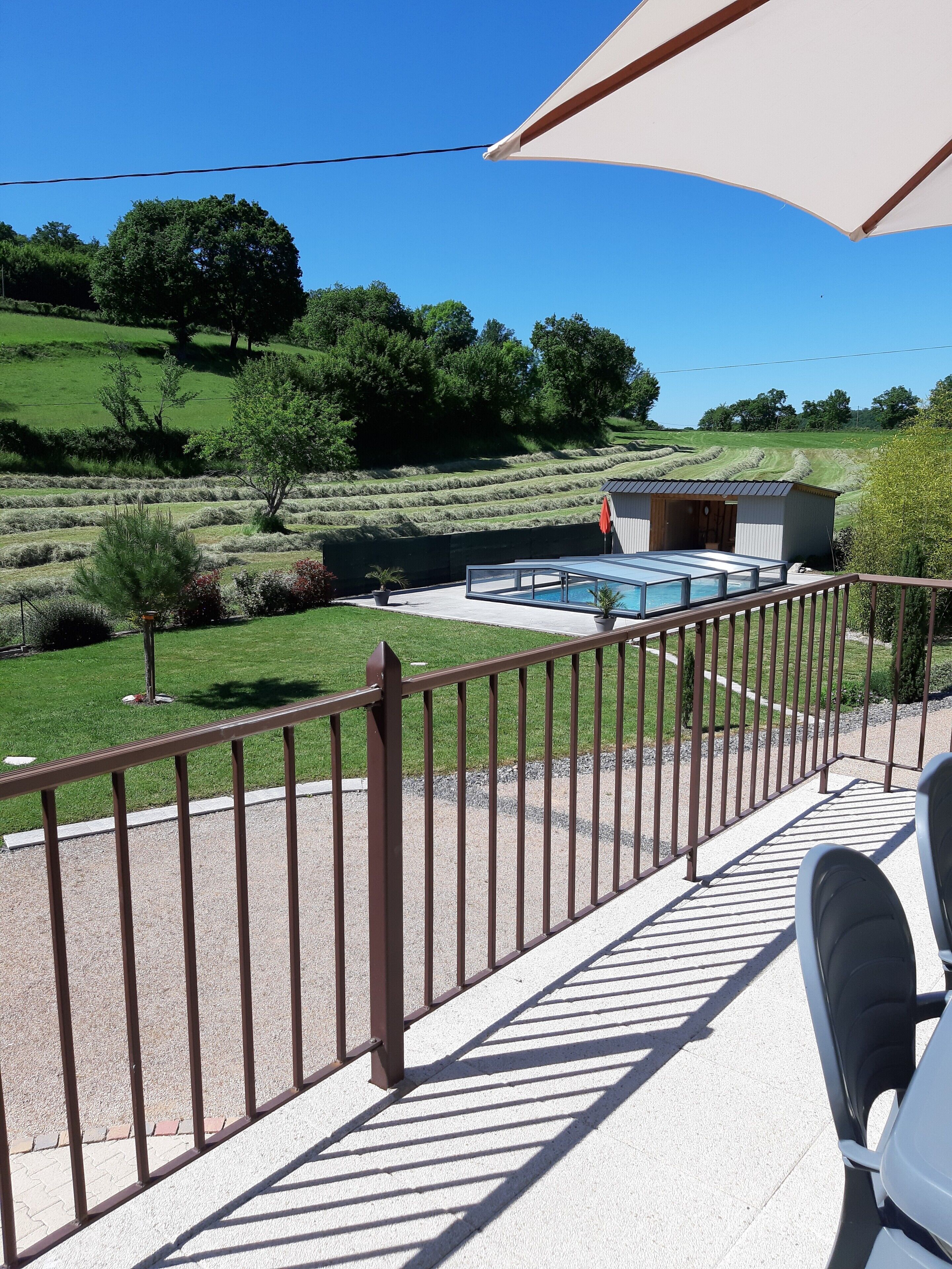 Une terrasse avec une piscine, un petit abri de jardin et une vue sur un paysage verdoyant.