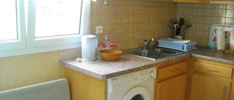 A compact kitchen with a washing machine, a sink, and wooden cabinets.