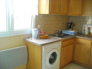 A compact kitchen with a washing machine, a sink, and wooden cabinets.