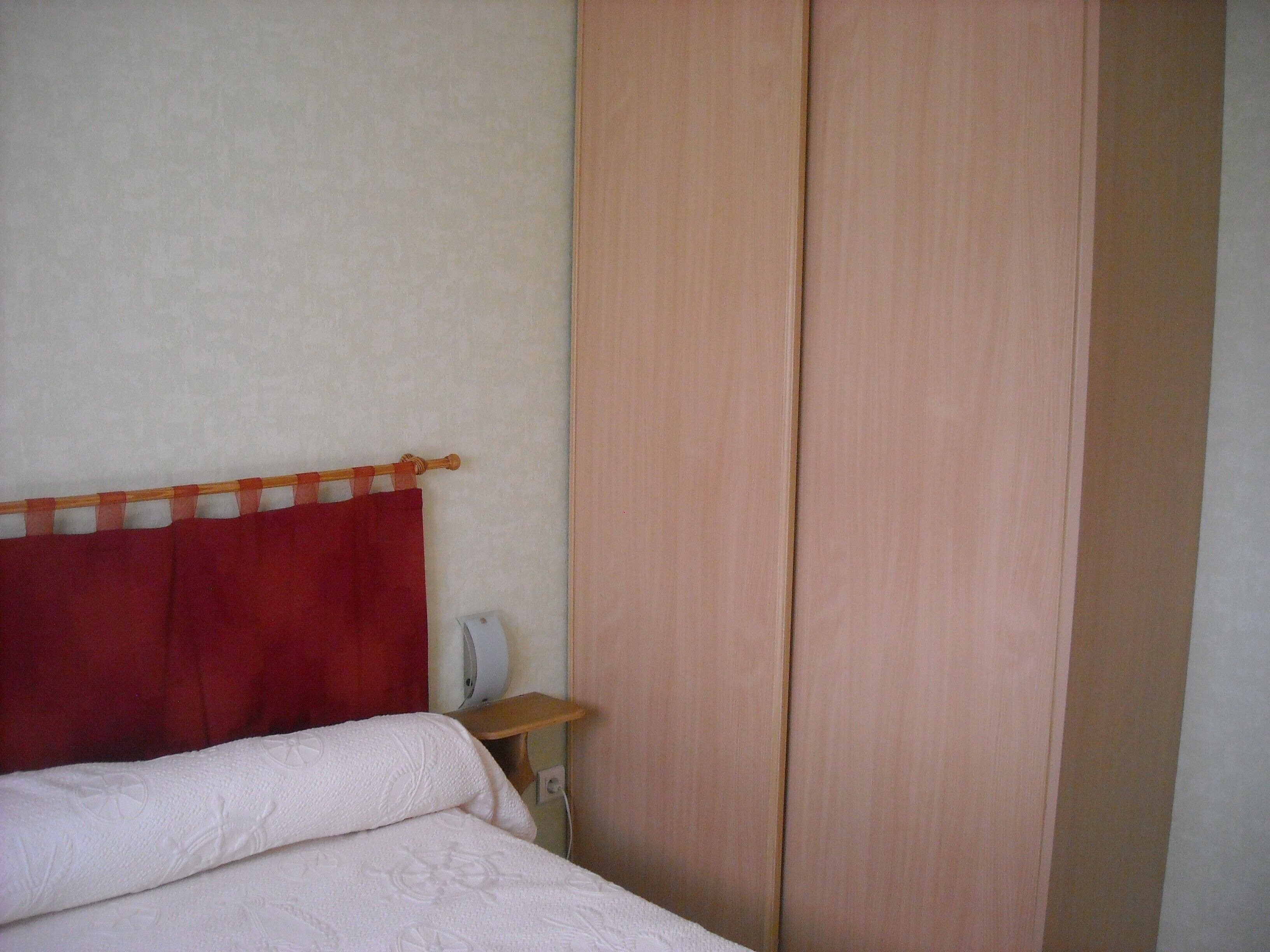 A bedroom with a bed, a wooden nightstand, a red curtain, and a wooden wardrobe.