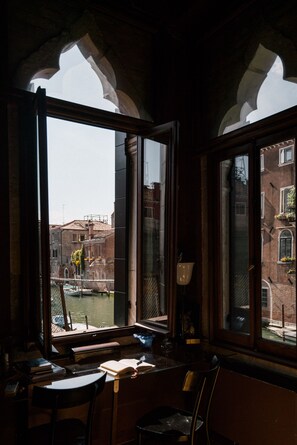 A room with a large window overlooking a canal, featuring a table and chairs, and a view of historic buildings. - Luxe and calm in sunny gothic palazzo Cannaregio (Venise)