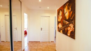 Un corridoio con porte bianche, pavimento piastrellato e un grande quadro appeso al muro.