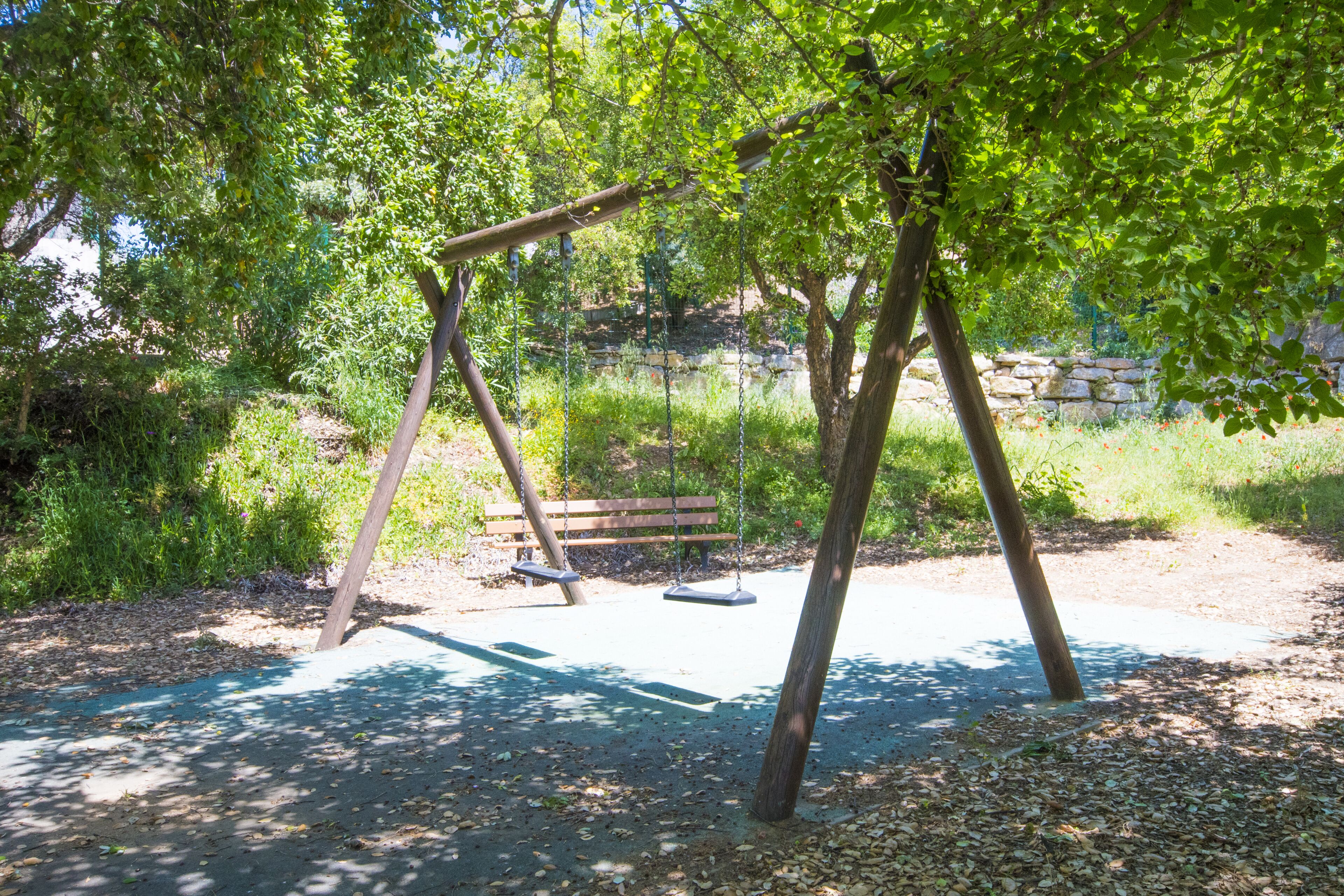 Un parque con un columpio, una banca y un muro de piedra al fondo.