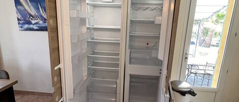 Una cocina con un refrigerador abierto, un cesto de basura y una mesa de comedor.