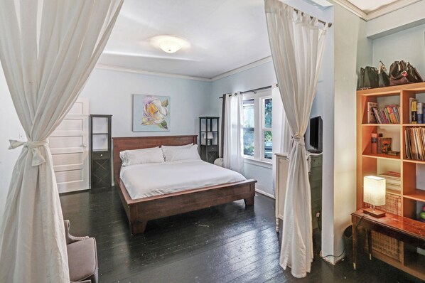 A bedroom with a wooden bed, white curtains, a bookshelf, and a painting on the wall. - Clean & Spacious-Walk to the Fairmont, great restaurants, coffee shops and wine (Sonoma)