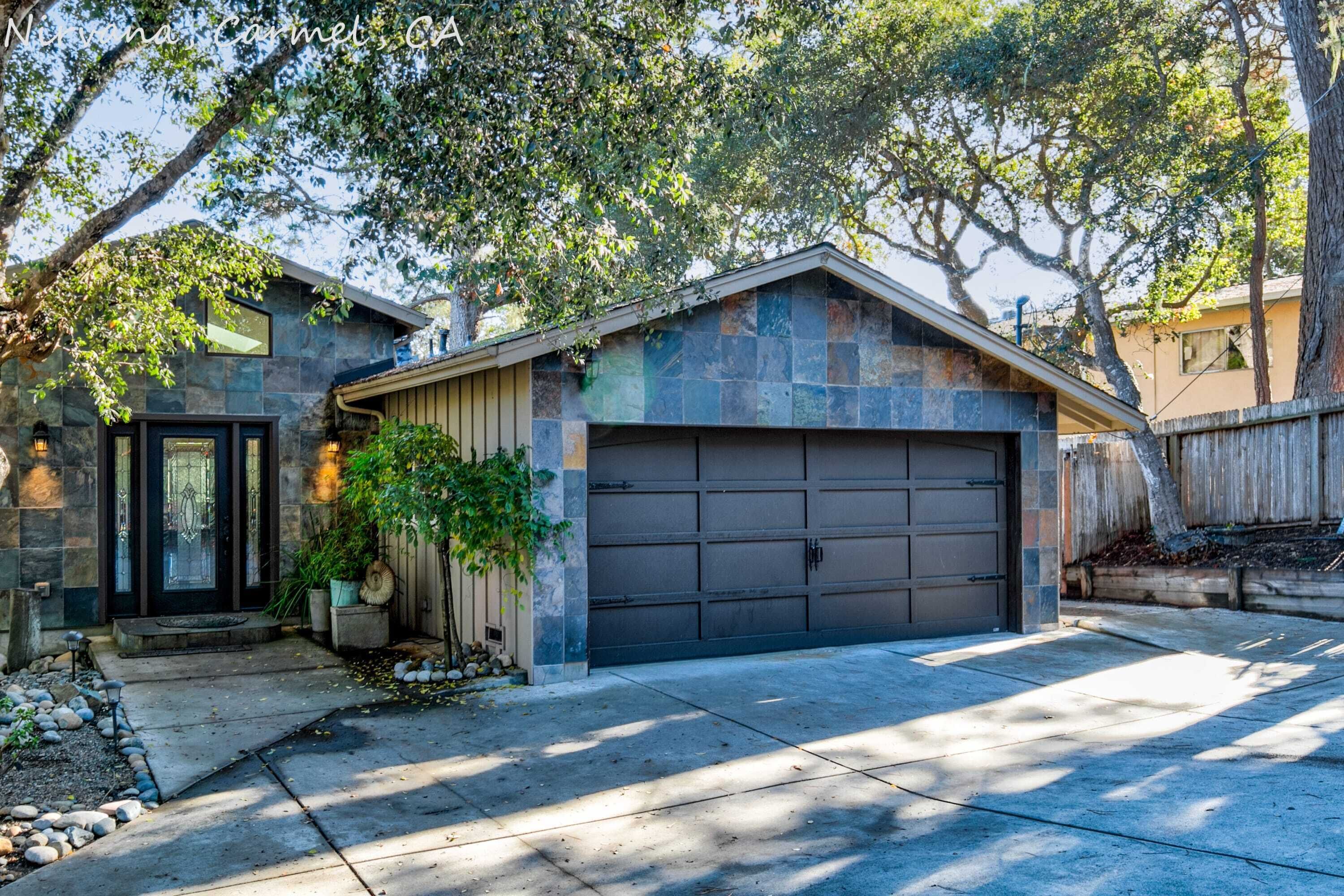 A modern house with a stone facade, a dark garage door, and a well-maintained front yard with a small tree and a potted plant.