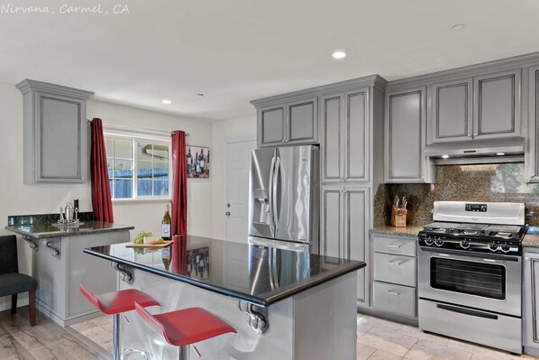 A modern kitchen with grey cabinets, stainless steel appliances, and a central island with red bar stools.