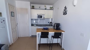 Un espacio habitable compacto con kitchenette, una zona de comedor con dos sillas y un sofá.